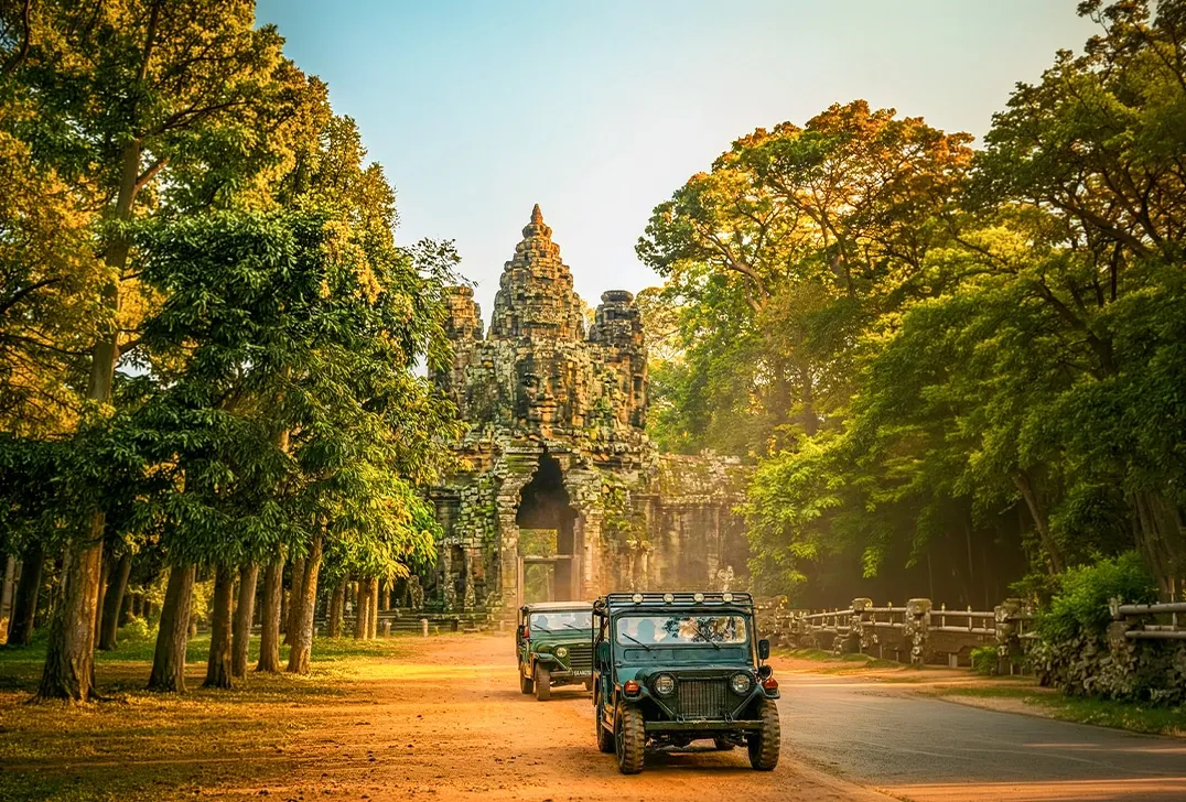 Jeep driving through ancient Angkor Wat temple ruins surrounded by lush trees in Cambodia